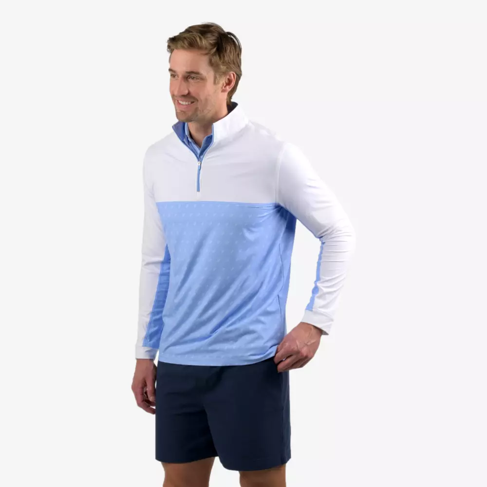A man stands smiling, wearing a white and light blue quarter-zip pullover and dark blue shorts against a plain light background—showcasing one of the best golf deals for around $250.