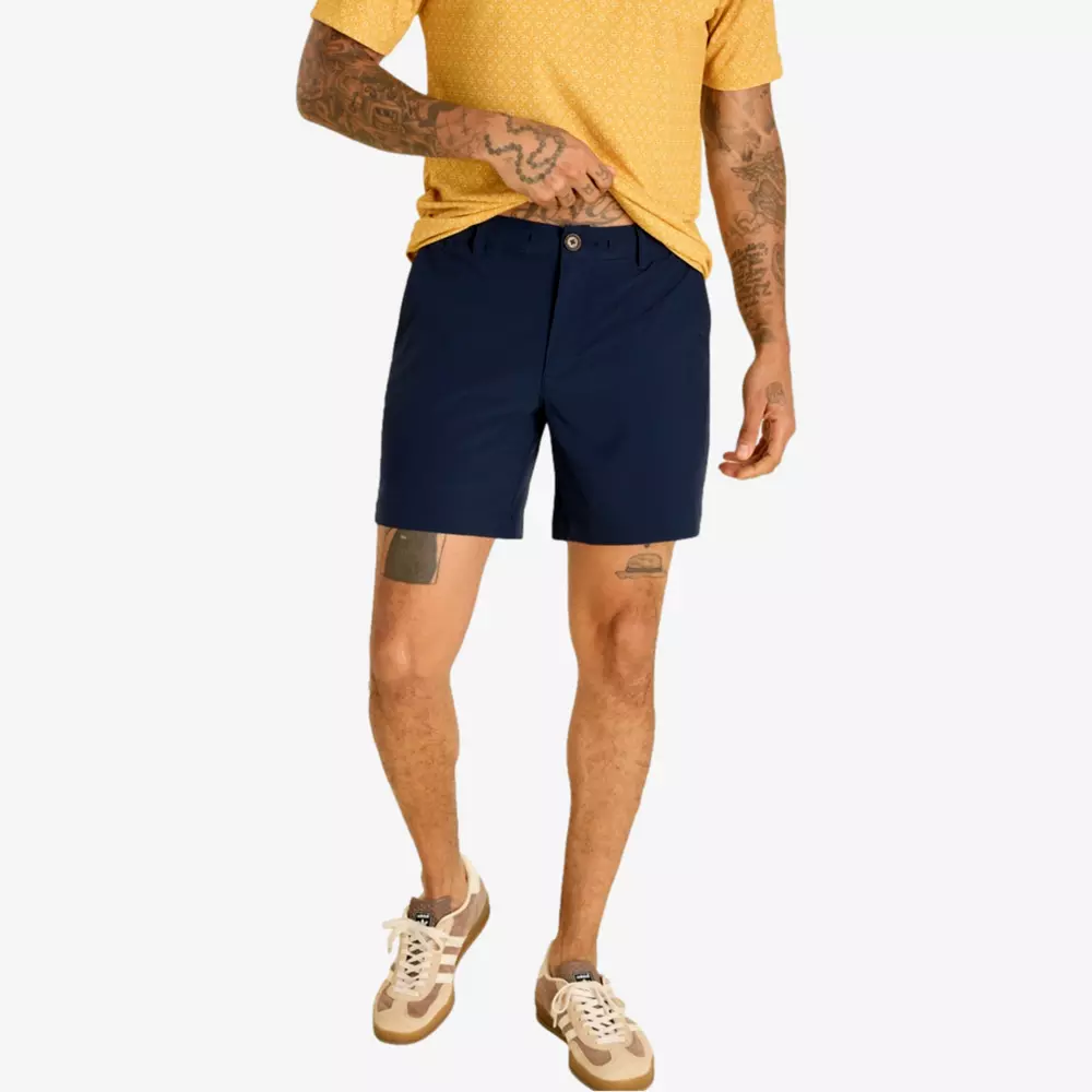 A person wearing a yellow patterned shirt, navy blue shorts, and beige sneakers stands against a white background. Stylish tattoos on their arms and legs reflect individuality—perfect inspiration for those seeking the best golf deals for around $250.