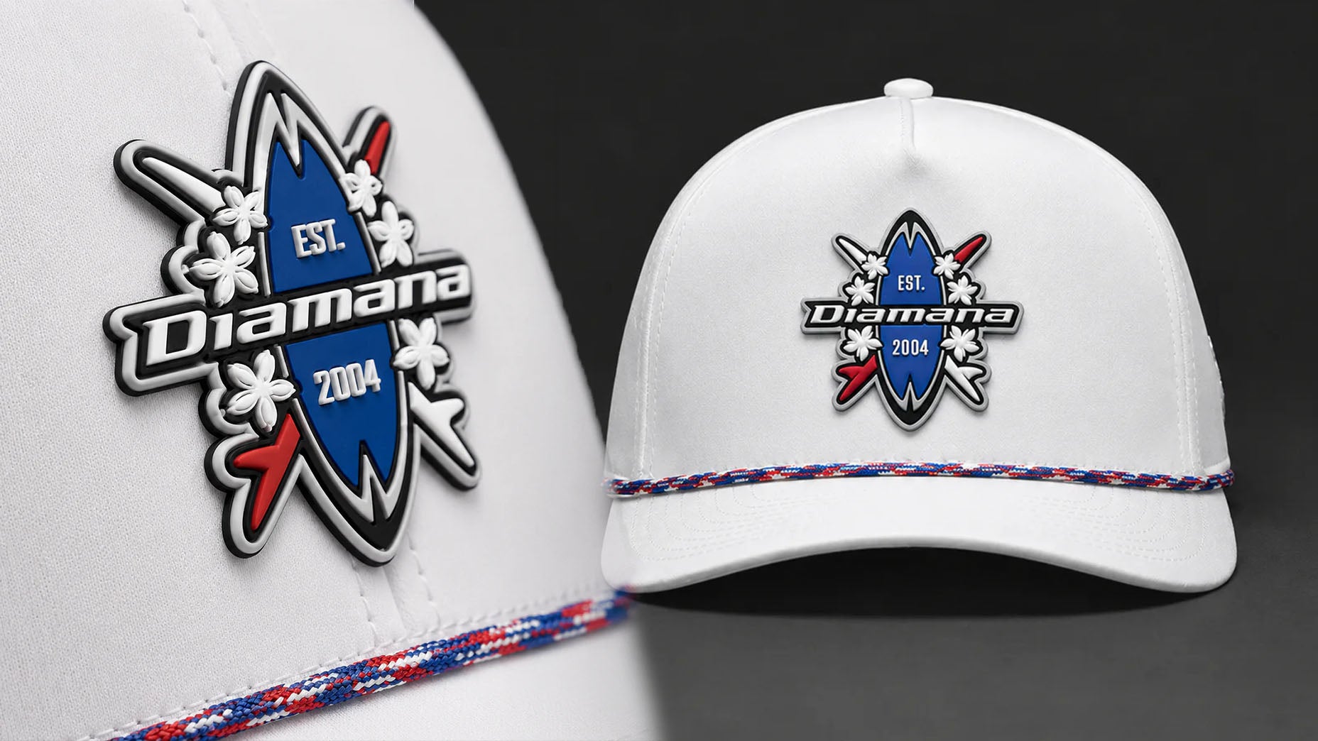 A white cap from the Red White and Blue collection features a blue surfboard-shaped Mitsubishi Diamana logo, EST. 2004, white flowers, and red arrows. A red, white, and blue braided band decorates the brim—perfect for the US Open.