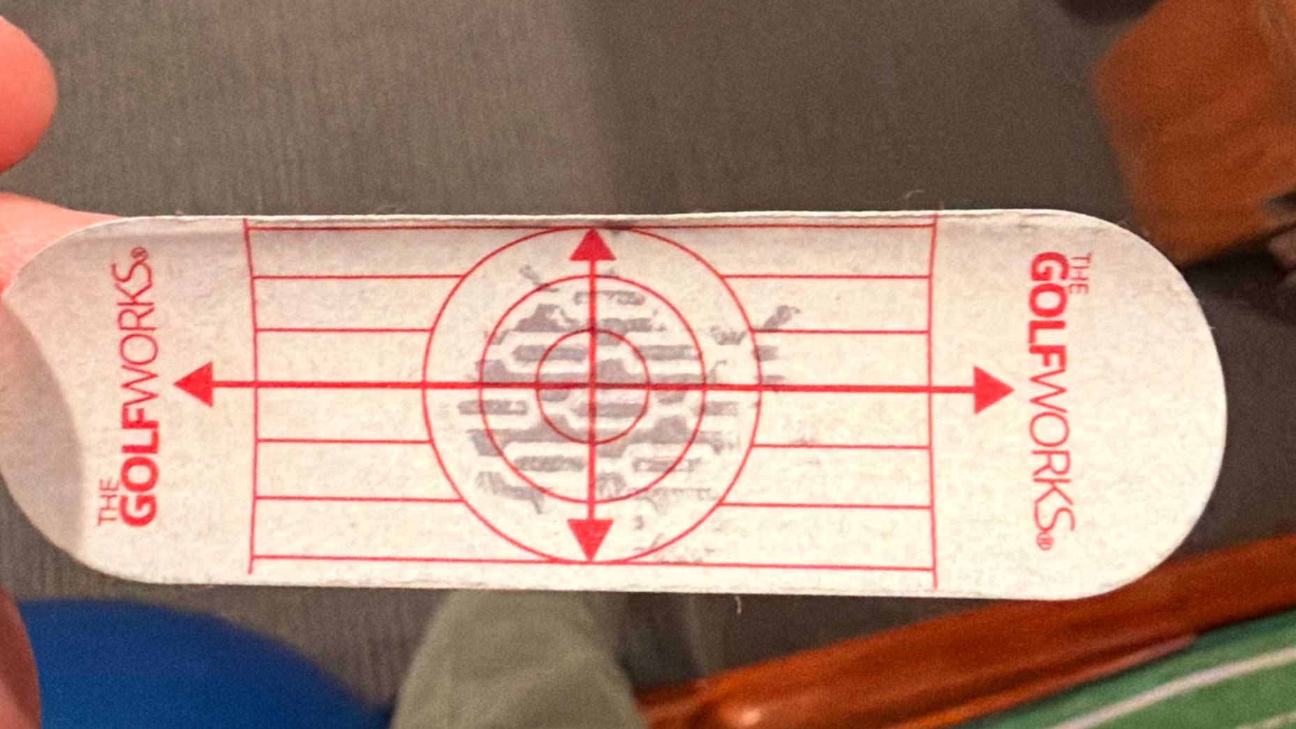 A rectangular adhesive golf impact tape from The GolfWorks features red target lines and a smudged mark in the center, making it easy to analyze your strike and optimize your zero-torque swing for greater consistency.