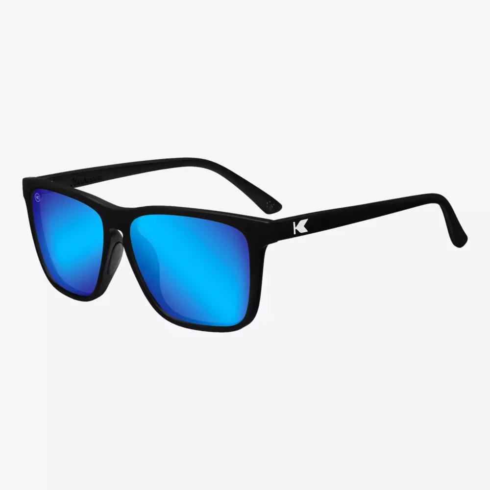 Black sunglasses with bright blue mirrored lenses, featuring a small white K logo on the arms, displayed on a plain white background.