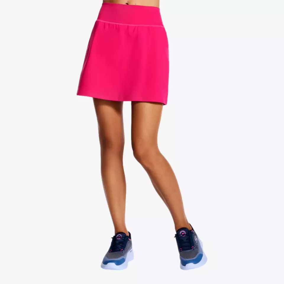 A person wearing a bright pink athletic skirt and navy blue Skechers stands against a plain white background. The upper body is not visible.