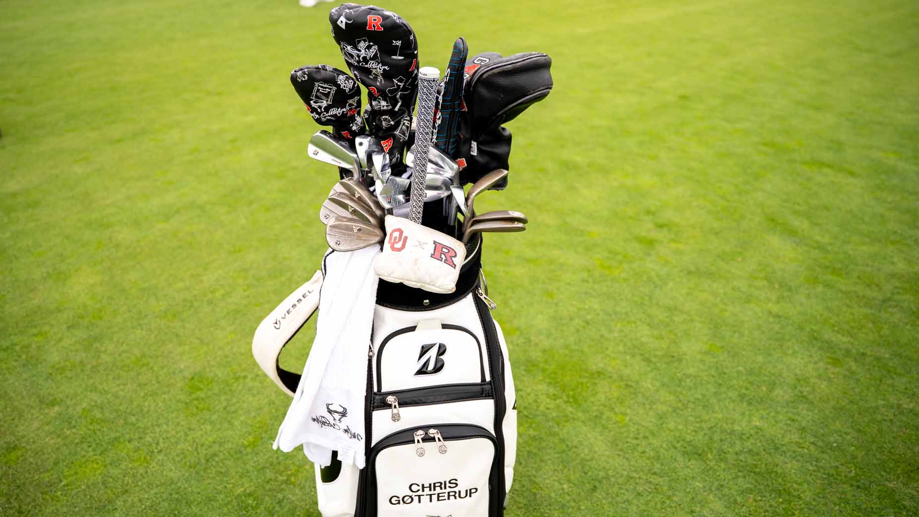 A white golf bag with Chris Gotterup printed on it stands on green grass, showcasing his Chris Gotterup WITB picks—various clubs, headcovers, and a white towel hanging on the side.