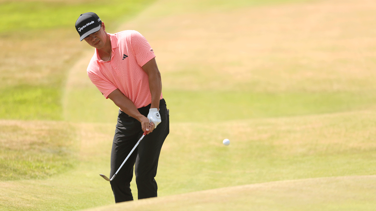A golfer in a pink shirt and black pants chips a golf ball onto the green during a sunny day on the golf course, capturing one of the Thursday highlights from the Open Championship that fans won't want to miss.