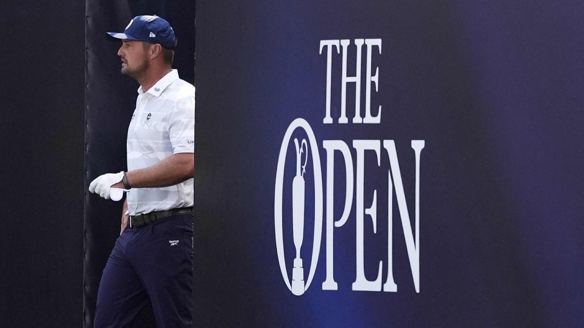 A golfer in a white shirt and blue cap stands next to a large sign that reads THE OPEN with a golf tee design inside the letter O.