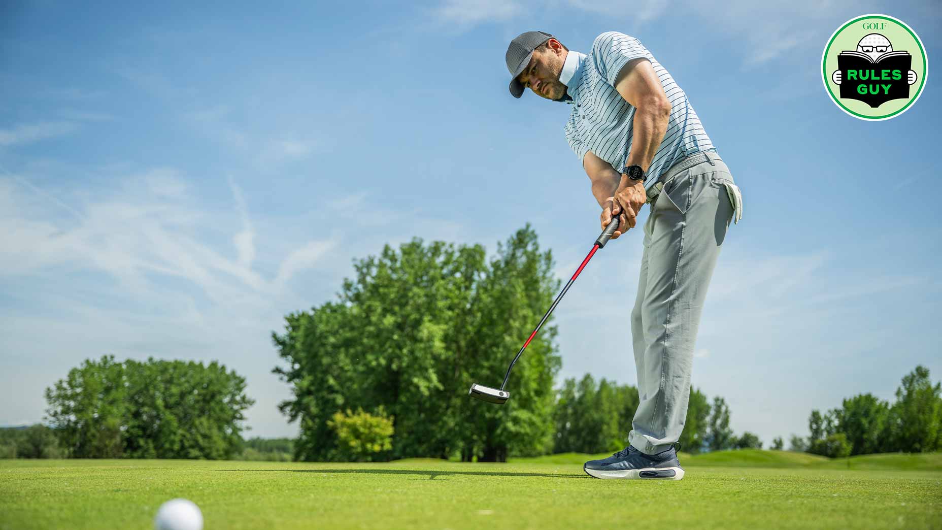 A man wearing a cap and sunglasses lines up his putter and putts a golf ball on a green course under a blue sky, with trees in the background and a Rules Guy golf logo in the top-right corner.